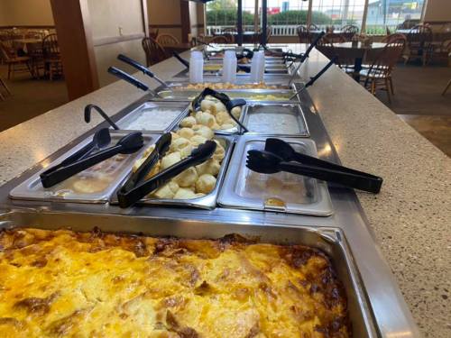 A buffet table featuring various dishes, including casseroles and rolls, with serving utensils and empty cups.