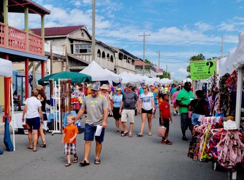 A bustling outdoor market with vendors, colorful tents, and people shopping on a sunny day.
