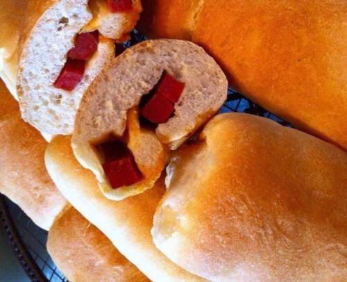 Freshly baked bread rolls with pieces of red meat inside, arranged on a cooling rack.
