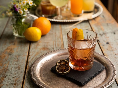 A cocktail in a crystal glass garnished with a citrus twist, resting on a slate plate with dried lemon slices.