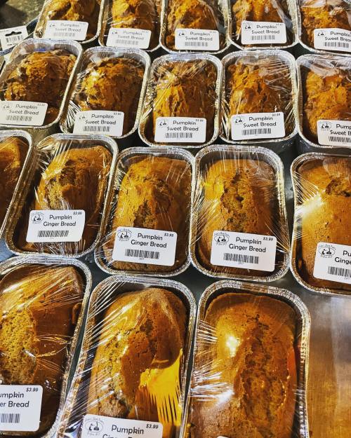 A display of multiple loaves of pumpkin ginger bread in clear plastic containers, each labeled with a price.