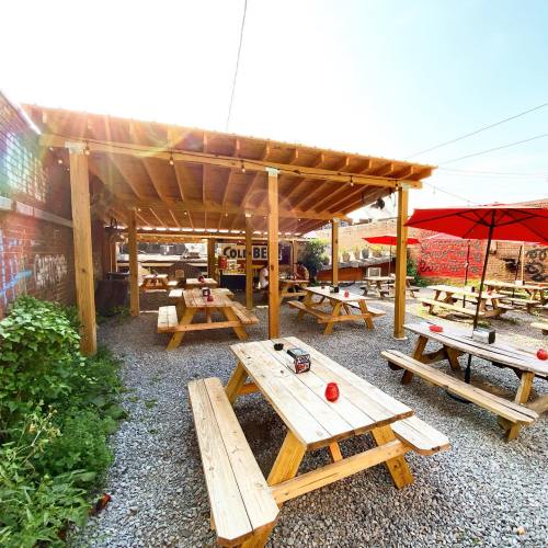 Outdoor dining area with wooden tables and benches, surrounded by greenery and colorful murals on the walls.