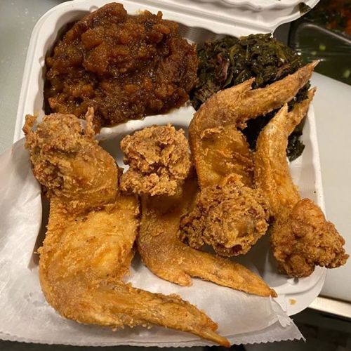 A takeout container with fried chicken wings, collard greens, and a serving of sweet potato casserole.