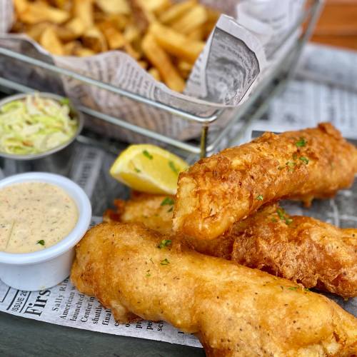 A plate of golden fried fish with a side of coleslaw, lemon, dipping sauce, and crispy fries in a basket.