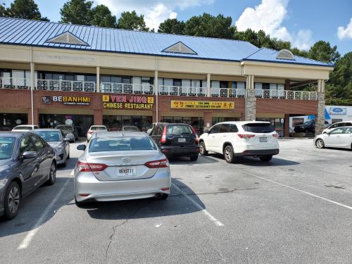 A parking lot in front of a two-story building with signs for a Chinese restaurant and a Vietnamese restaurant.