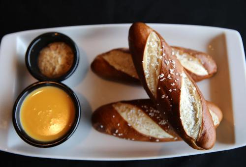 A plate with two soft pretzels, a small bowl of mustard, and a bowl of cheese dip.