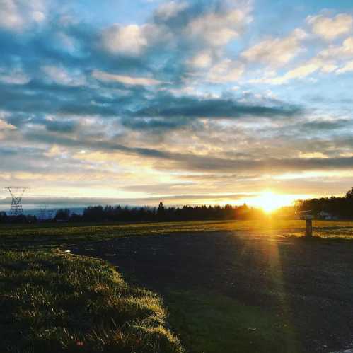 A serene landscape at sunset, with vibrant clouds and a glowing horizon over a grassy field.