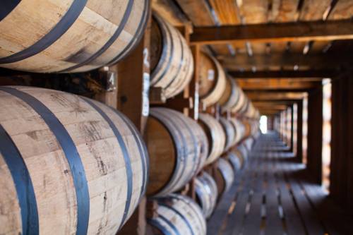 A row of wooden barrels stacked on shelves in a rustic storage area, with a blurred background.