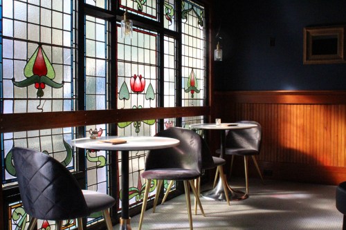 A cozy café corner with stained glass windows, small tables, and stylish chairs, bathed in soft natural light.