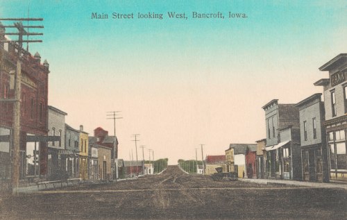 Vintage postcard of Main Street, Bancroft, Iowa, looking west, featuring buildings and a clear blue sky.