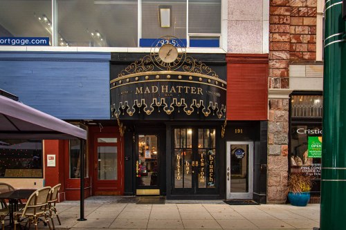 Exterior of the Mad Hatter Bar, featuring ornate signage and a clock above the entrance, in a colorful urban setting.