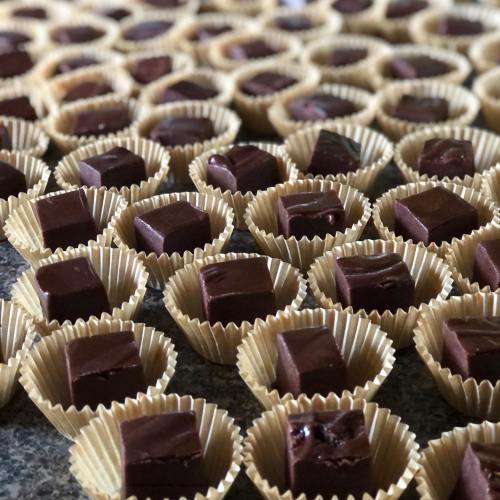 A close-up of numerous chocolate squares in small paper cups arranged on a surface.