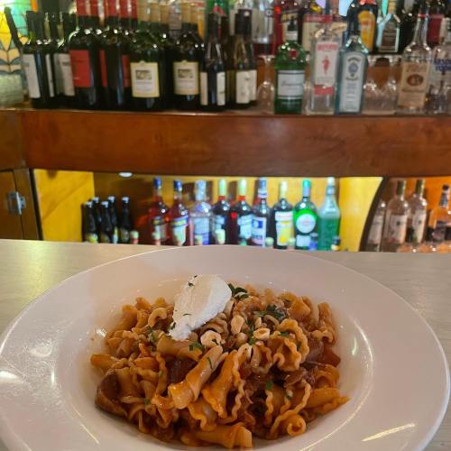 A plate of pasta topped with cream and herbs, with a bar filled with various bottles in the background.