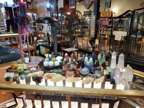 A display of various colorful crystals and gemstones arranged on a wooden counter in a shop.