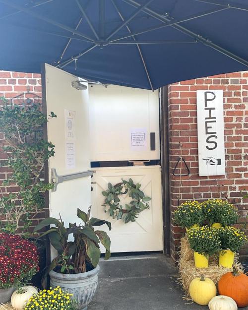 A welcoming entrance with a white door, decorated with a wreath, surrounded by potted plants and autumn decorations.