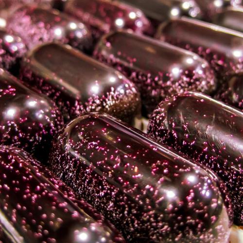 Close-up of shiny, dark purple capsules with a glittery texture, arranged closely together.