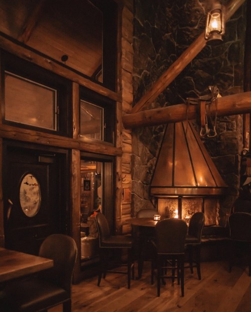 Cozy interior of a rustic lodge with a stone fireplace, wooden beams, and dim lighting.