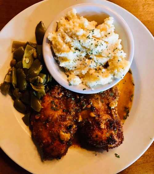 A plate featuring fried chicken, creamy mashed potatoes, and green beans, garnished with herbs.