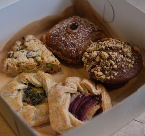 A box of assorted pastries, including a scone, muffin, and various flaky pastries with fillings.