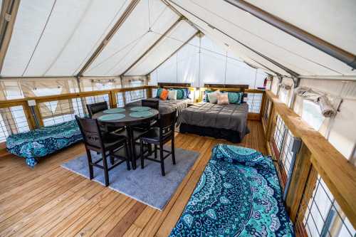 Cozy glamping tent interior with two beds, a dining table, and colorful decor on wooden flooring.