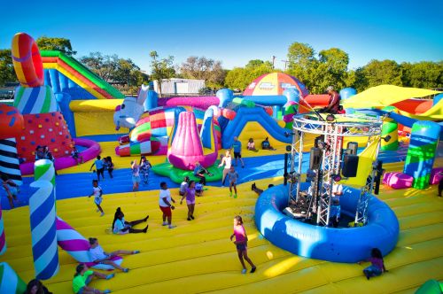 A vibrant inflatable playground filled with people enjoying various colorful bounce structures under a clear blue sky.