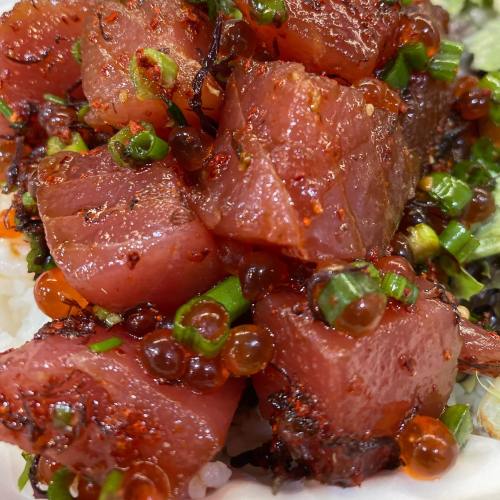 A close-up of diced marinated tuna on rice, garnished with green onions and orange fish roe.