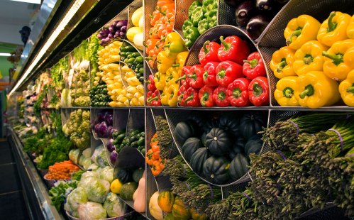 A vibrant display of assorted fresh vegetables, including peppers, squash, and leafy greens, in a grocery store.
