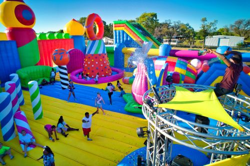 A vibrant inflatable playground with colorful slides and structures, filled with people enjoying a fun day outdoors.