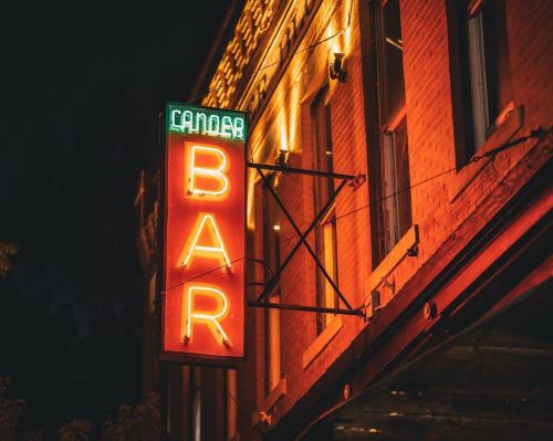 Neon sign for a bar illuminated at night, featuring bright red and green colors against a brick building.