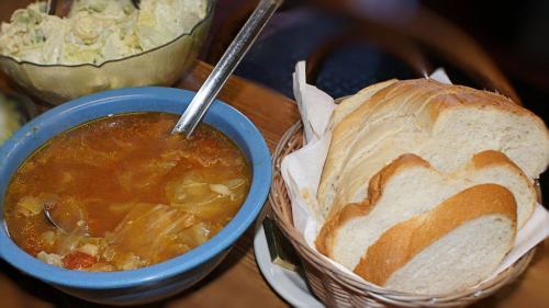 A bowl of soup with vegetables next to a basket of sliced white bread.