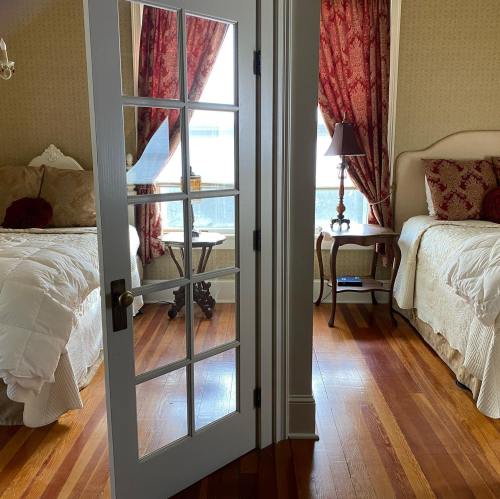 A cozy bedroom with two beds, a small table, and large windows, separated by a glass-paneled door.