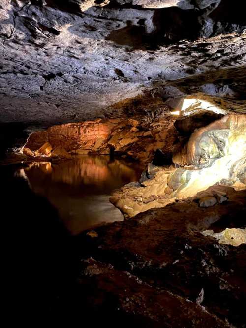 A dimly lit cave with rocky walls and a small pool of water reflecting light.