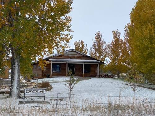 A log cabin surrounded by autumn trees, with a light dusting of snow on the ground and a sign in front.