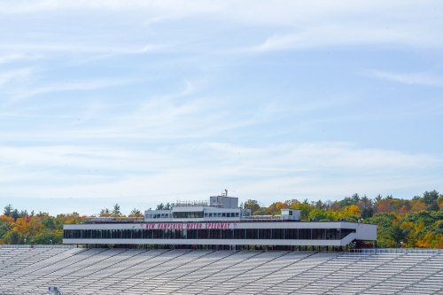 A grandstand at a racetrack surrounded by trees with autumn foliage under a clear blue sky.