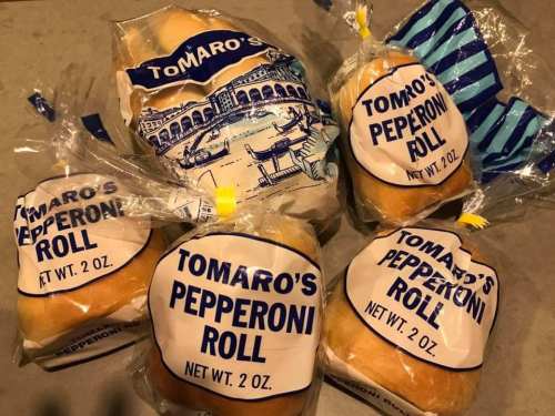 Four packages of Tomaro's Pepperoni Rolls, each labeled with a blue and white design, on a gray surface.