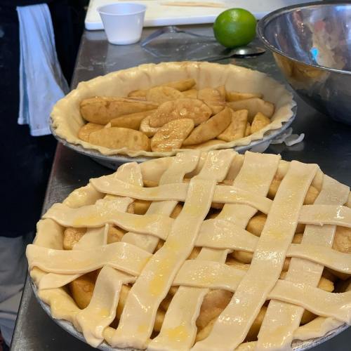 A countertop with two pie crusts: one filled with apple slices and the other topped with a lattice crust.