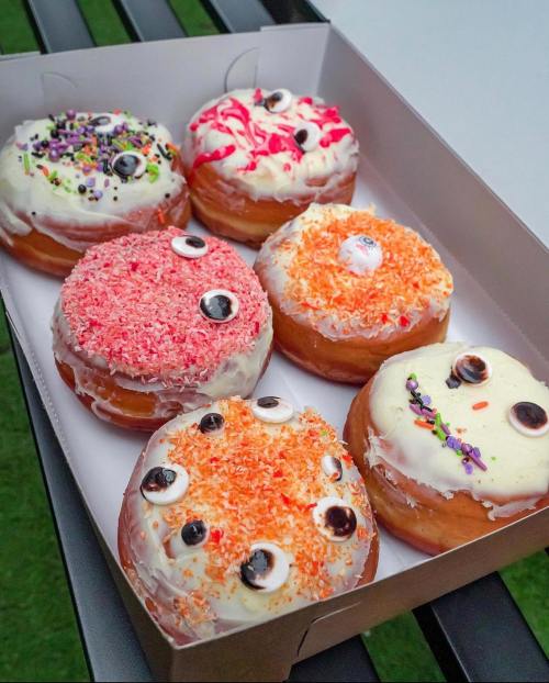 A box of six colorful donuts with various toppings, including sprinkles, frosting, and candy eyes.