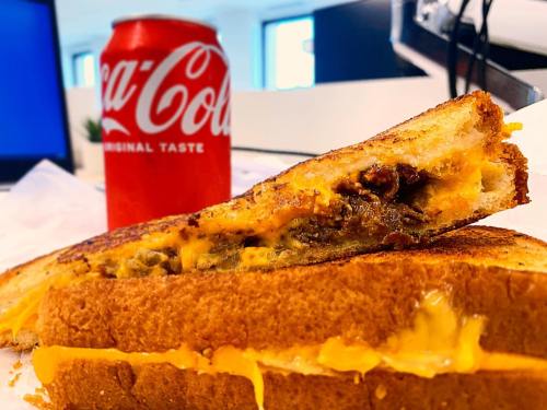A close-up of a grilled cheese sandwich with melted cheese, next to a can of Coca-Cola on a table.