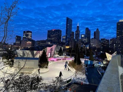 A winter scene featuring an ice skating rink surrounded by city skyscrapers under a twilight sky.