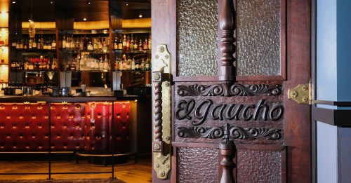 A wooden door with "El Gaucho" carved into it, leading to a stylish bar with a warm ambiance.