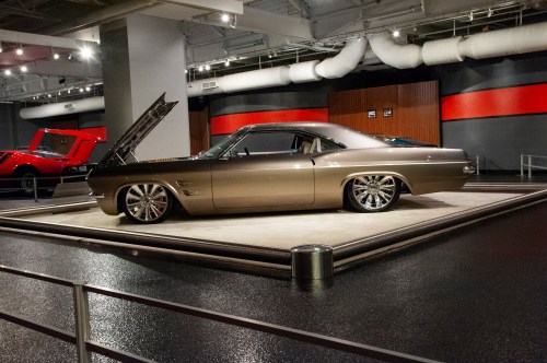 A sleek, vintage car displayed in a modern showroom with an open hood and polished chrome wheels.