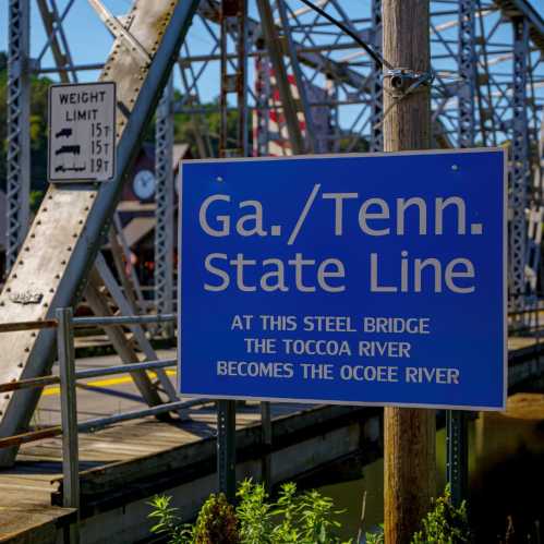 Sign marking the Georgia/Tennessee state line at a steel bridge, with the Toccoa River becoming the Ocoee River.