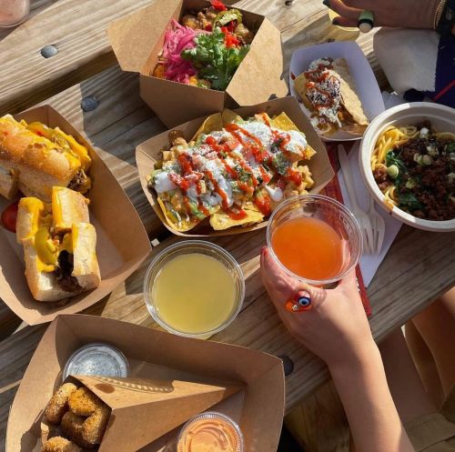 A variety of colorful dishes on a wooden table, including hot dogs, nachos, pasta, and drinks.