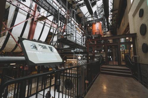 Interior view of a museum with industrial architecture, featuring metal structures, exhibits, and a staircase.