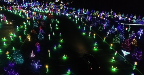 Aerial view of a festive display with colorful illuminated trees and decorations in a dark parking lot.
