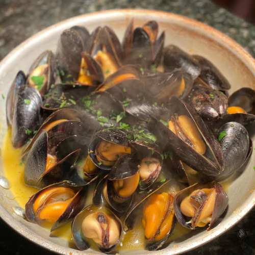A bowl of steaming mussels garnished with herbs in a flavorful broth.