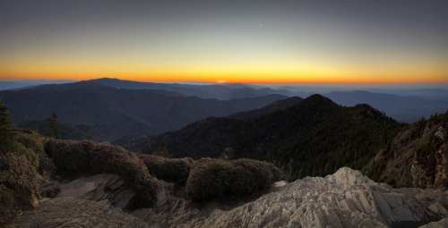 A panoramic view of mountains at sunset, with a gradient sky transitioning from orange to deep blue.