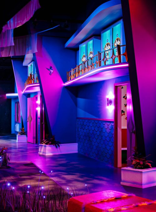 Colorful, whimsical building exterior with blue walls, vibrant lighting, and decorative windows.