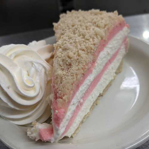A slice of layered cake with pink and white frosting, topped with a dollop of whipped cream on a plate.
