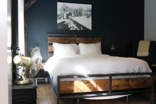 Cozy bedroom with a wooden bed, white bedding, a vintage fan, and a black wall featuring a landscape photo.